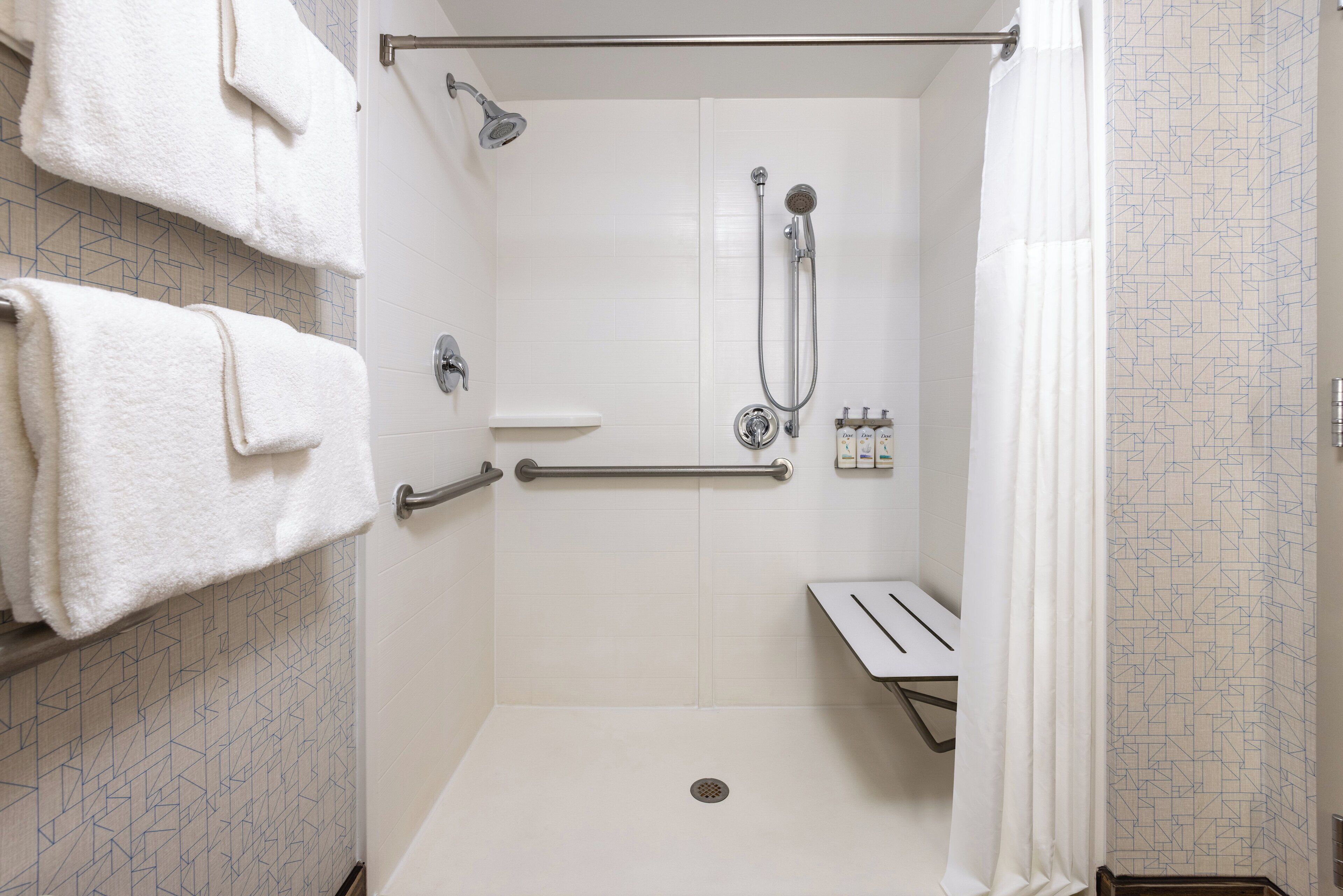 A walk-in shower with a grab bar, a handheld showerhead, and a handheld faucet.