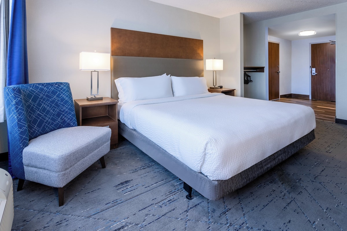 Ein Hotelzimmer mit einem großen Bett, einem Sessel, zwei Nachttischen mit Lampen und einem Holzkopfteil.