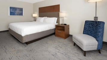 Une chambre d’hôtel avec un grand lit, une table de chevet avec une lampe, une chaise et une lampe fixée au mur.