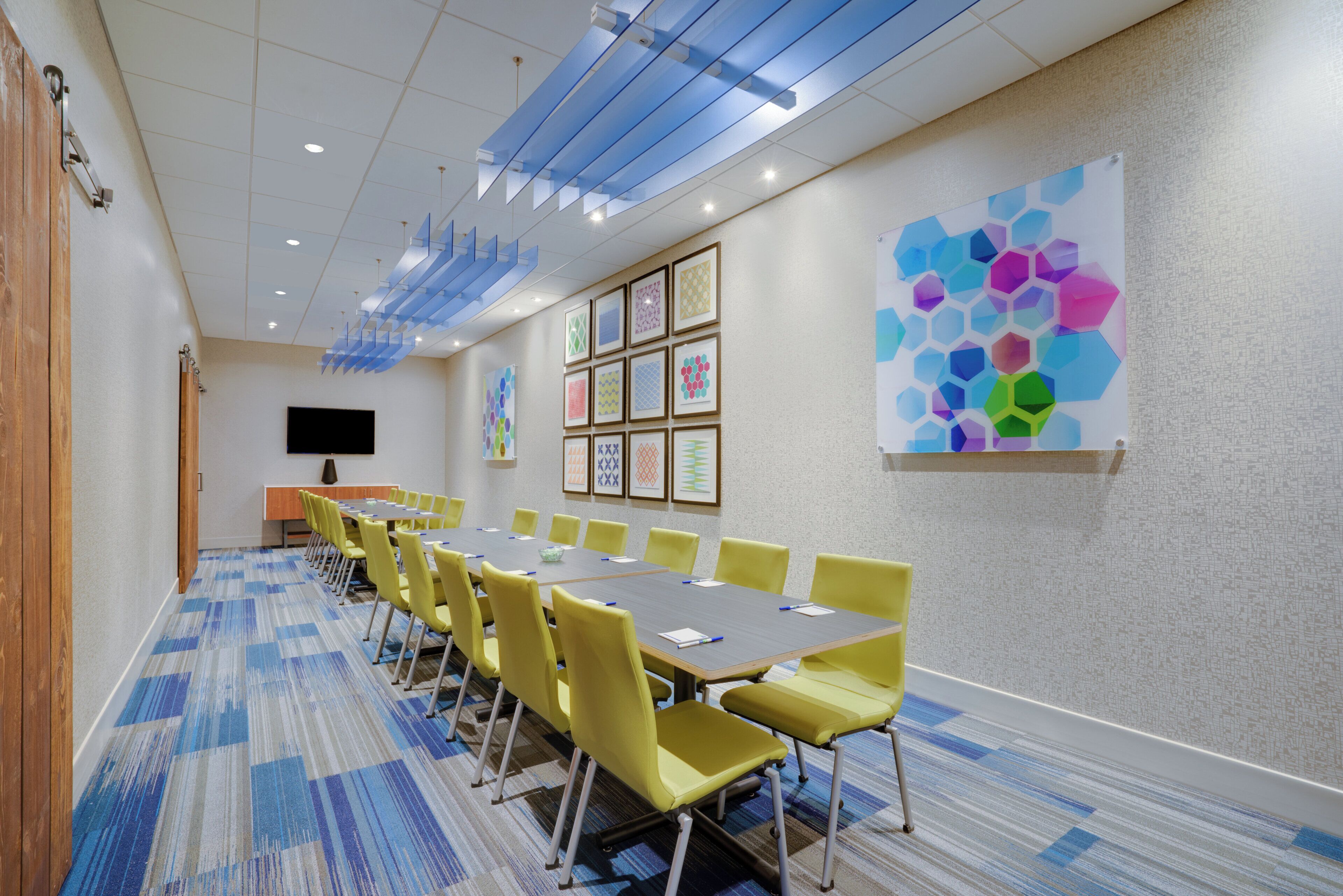 A conference room with a long table, yellow chairs, and a large abstract painting on the wall.