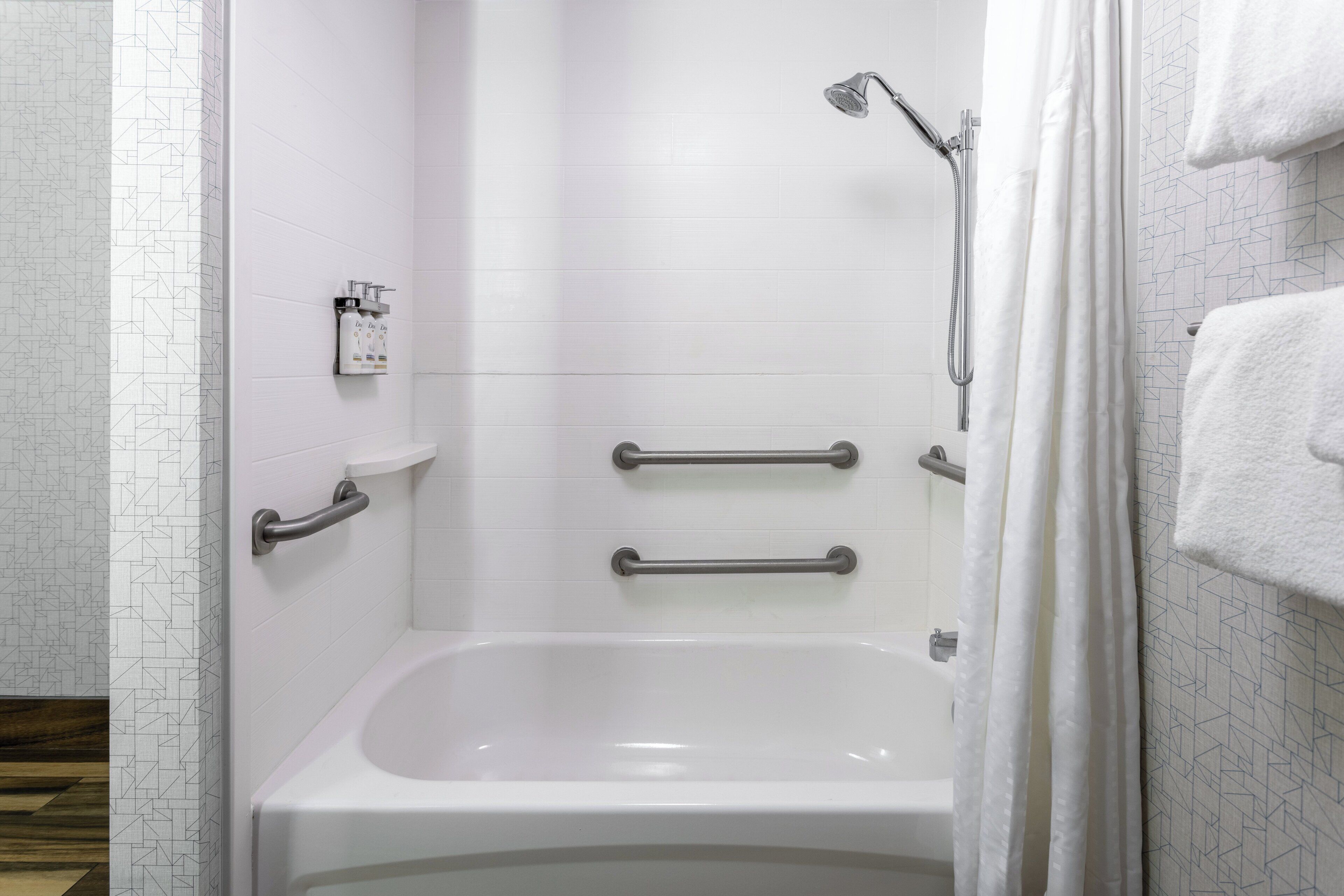A modern bathroom with a white bathtub, grab bars, and a showerhead.