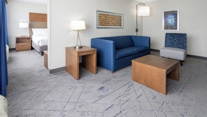Una habitación de hotel con cama, sofá azul, una mesita, lámpara y una silla.
