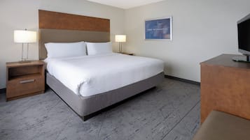 A hotel room with a large bed, two bedside tables with lamps, a flat-screen TV, and a framed picture on the wall.