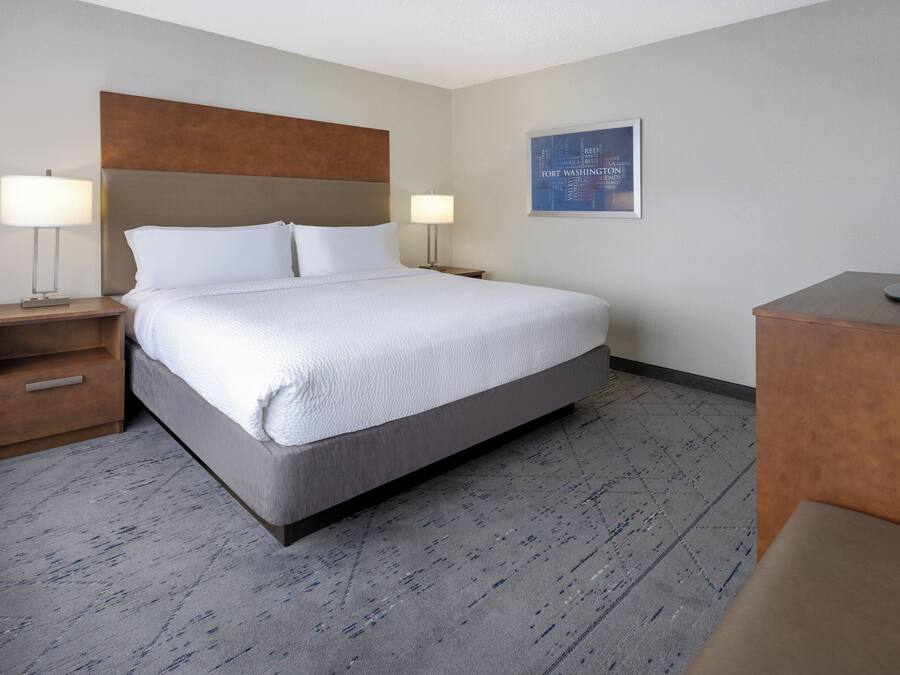 A hotel room with a large bed, two bedside tables with lamps, a flat-screen TV, and a framed picture on the wall.