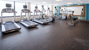 Un gimnasio con cintas de correr, bicicletas estáticas y un espejo grande.