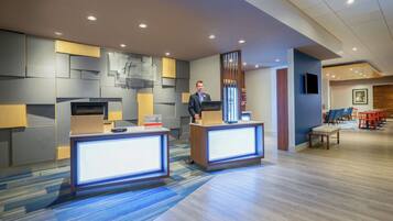A modern hotel reception area with two reception desks, a seating area with chairs, and a television mounted on the wall.