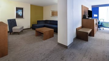 Une chambre d’hôtel comprenant un canapé d’angle, un petit fauteuil, une table basse et un bureau avec un téléviseur.
