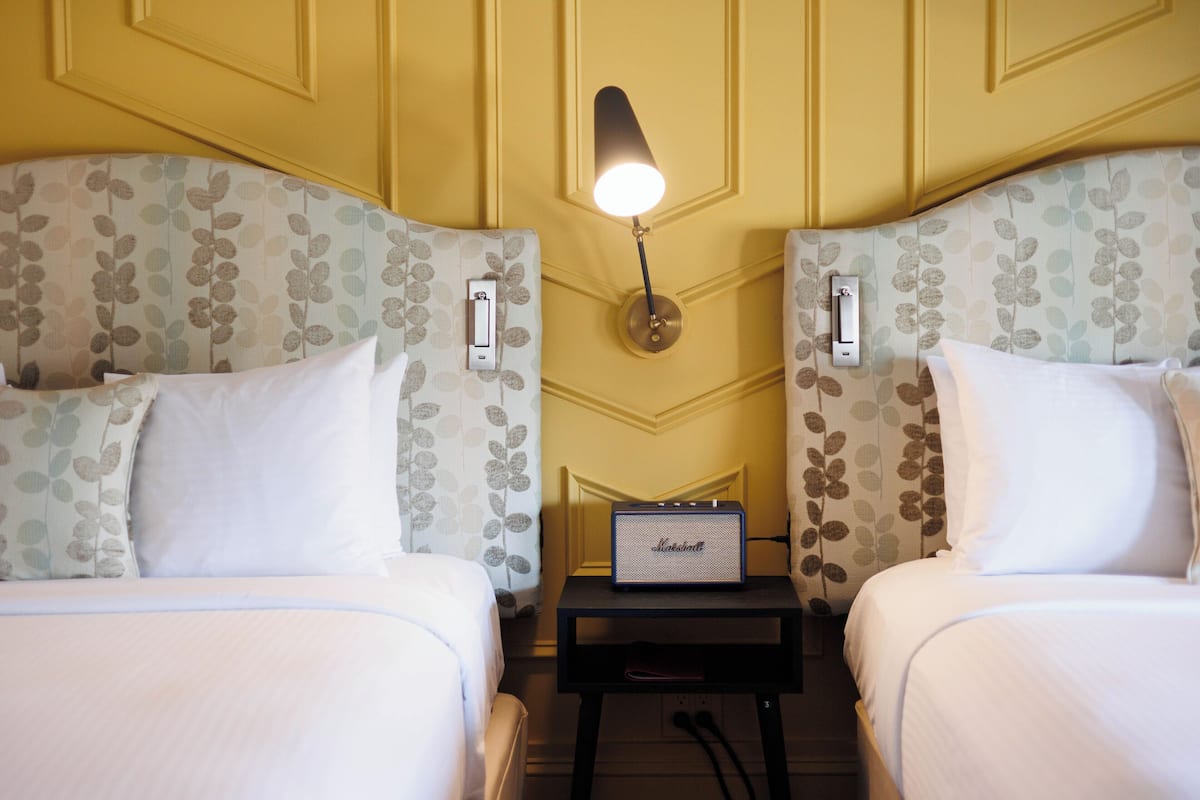 A hotel room with two beds, a nightstand with a lamp, and a sign indicating a minibar.