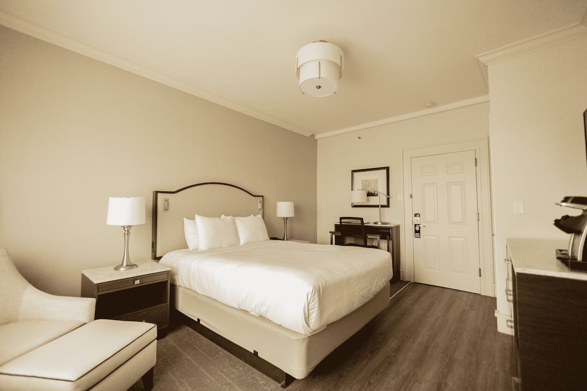 A hotel room with a bed, a chair, a desk, and a wardrobe.