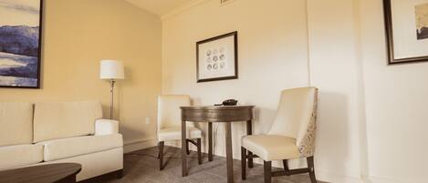 A hotel room with a sofa, two chairs, a small table, a lamp, and two framed pictures on the wall.