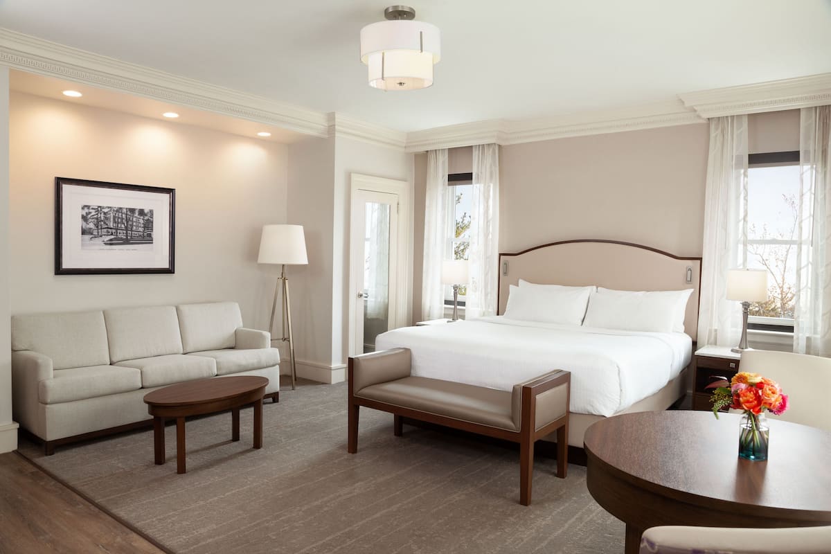A hotel room with a bed, a sofa, a coffee table, and a dining table.