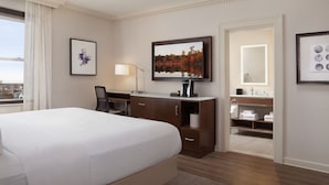 Habitación de hotel con una cama grande, un escritorio con silla, televisor, espejo y vista a la ciudad.