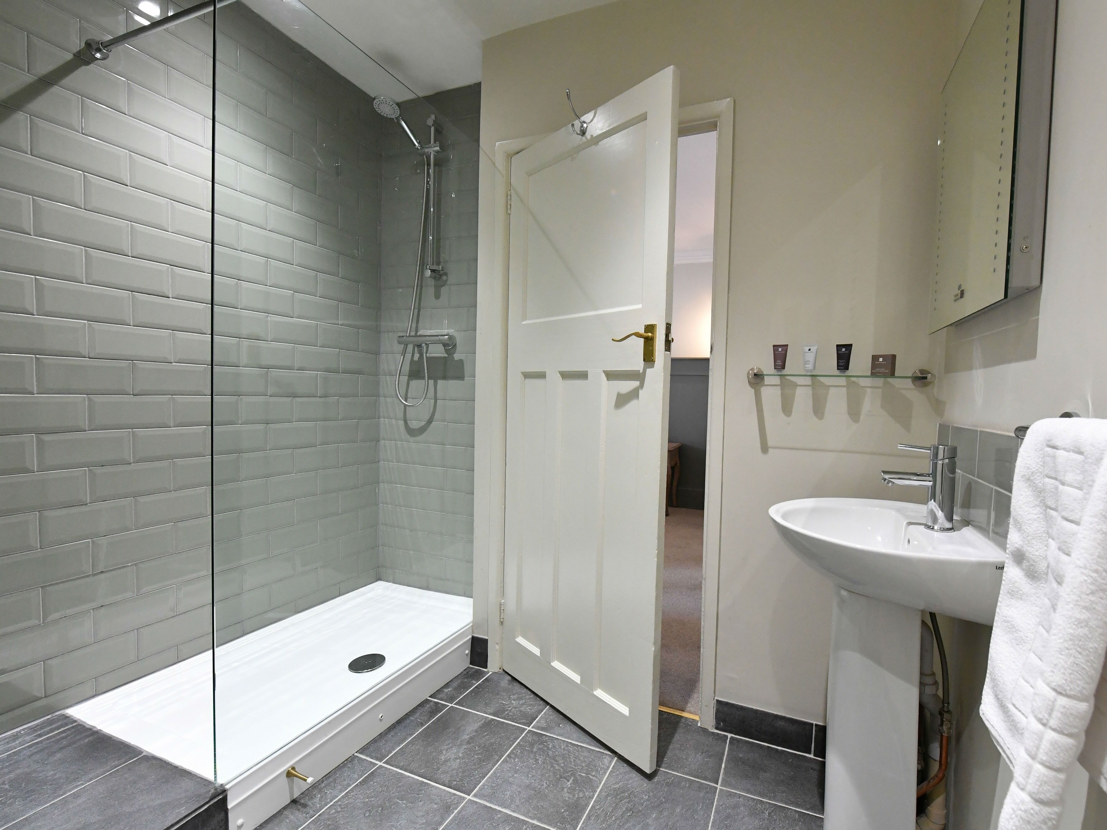 Un baño moderno con cabina de ducha de vidrio, un lavamanos blanco y un perchero para toallas.