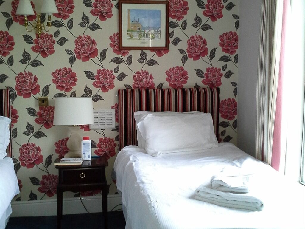 A hotel room with a bed, a nightstand, a lamp, a framed picture on the wall, and a window with curtains.