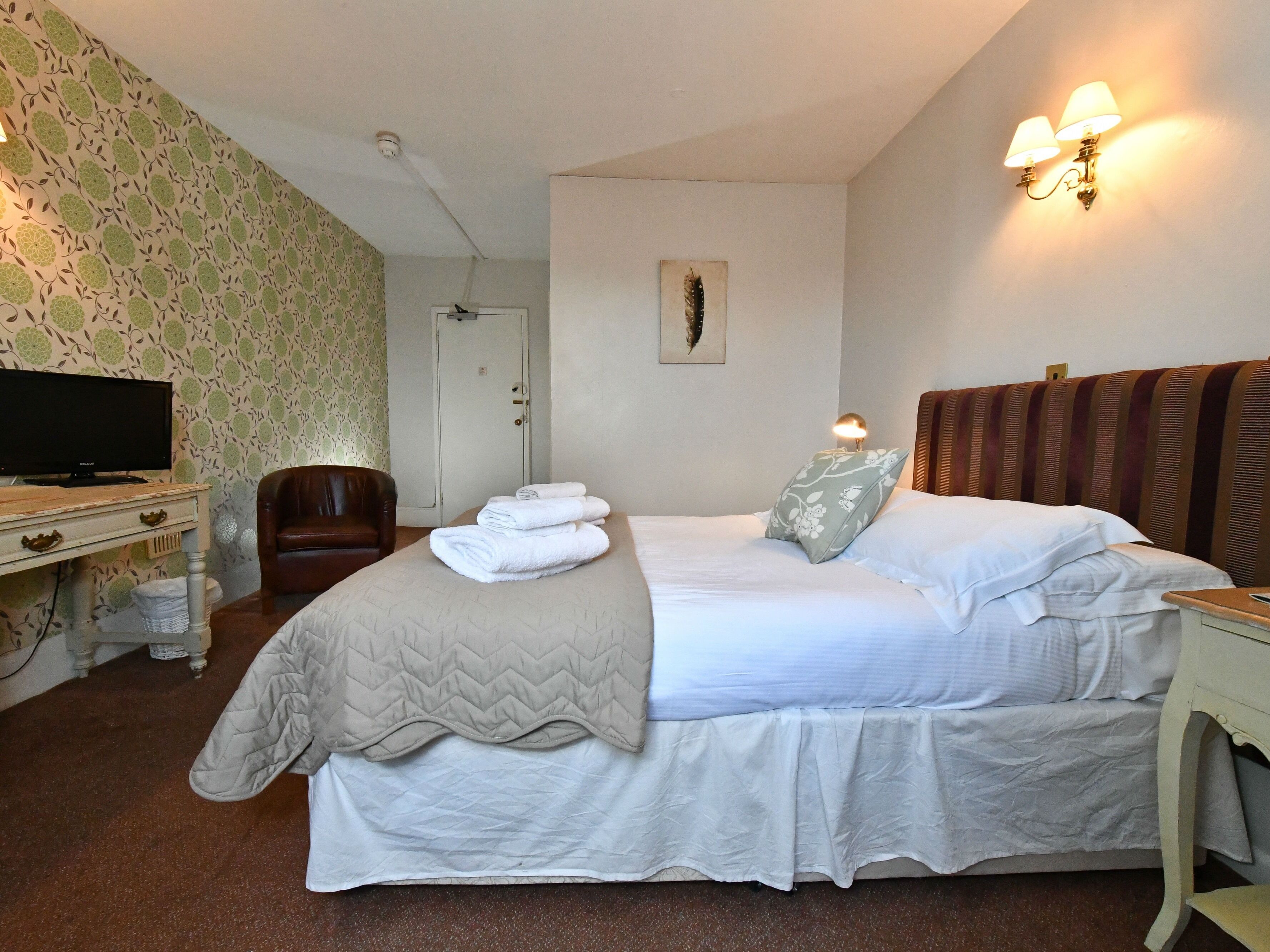 Habitación de hotel ordenada con cama, una silla, televisor y lámpara fijada a la pared.