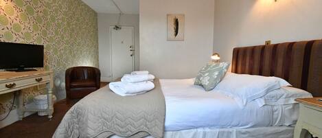 Habitación de hotel ordenada con cama, una silla, televisor y lámpara fijada a la pared.