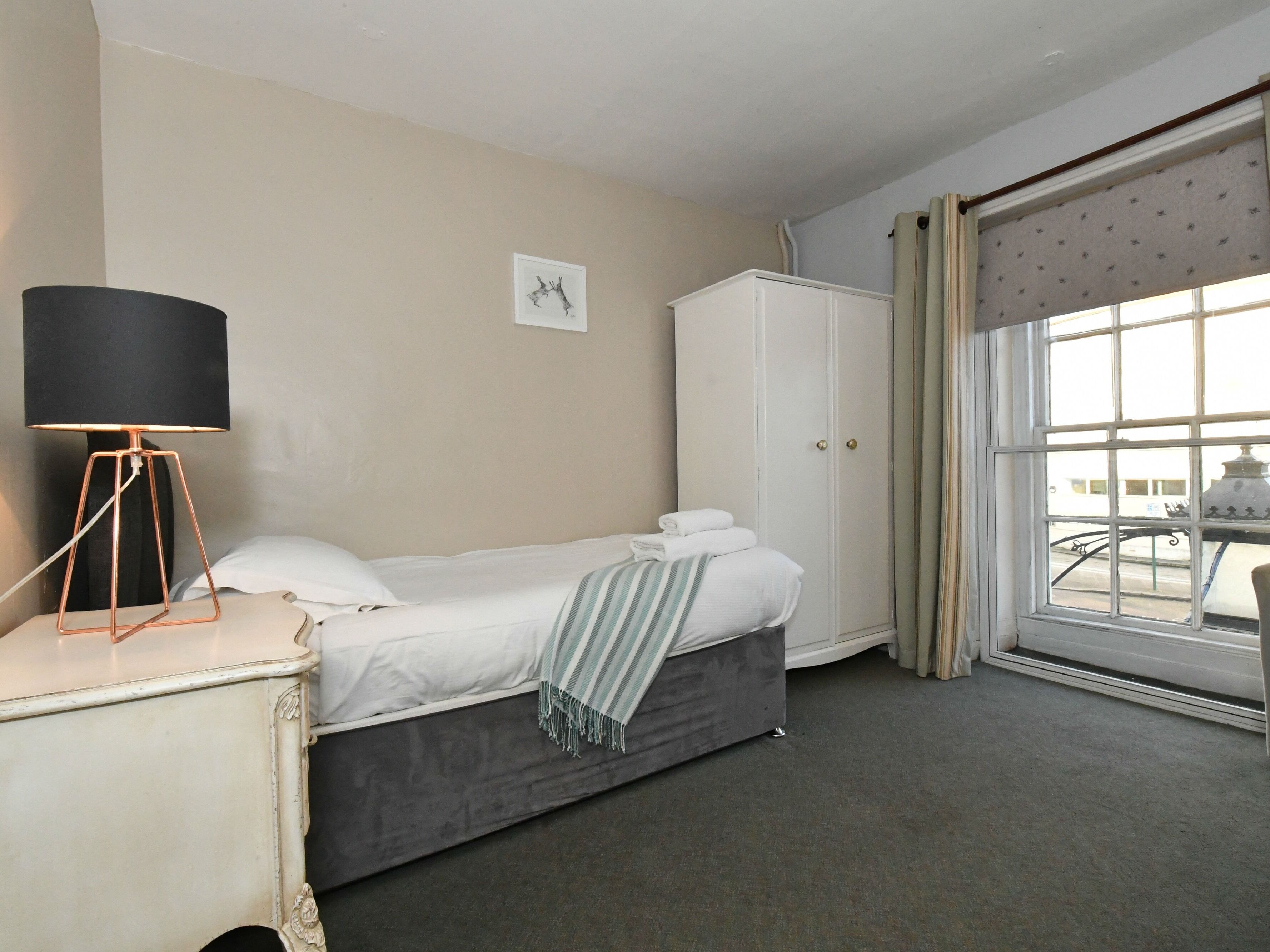 Una habitación de hotel con una cama, una mesita de noche con lámpara, un armario y una ventana con cortinas.