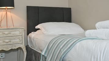 Uma cama bem arrumada com lençóis brancos e um cobertor listrado, uma luminária de cabeceira e uma mesinha de cabeceira de estilo vintage.