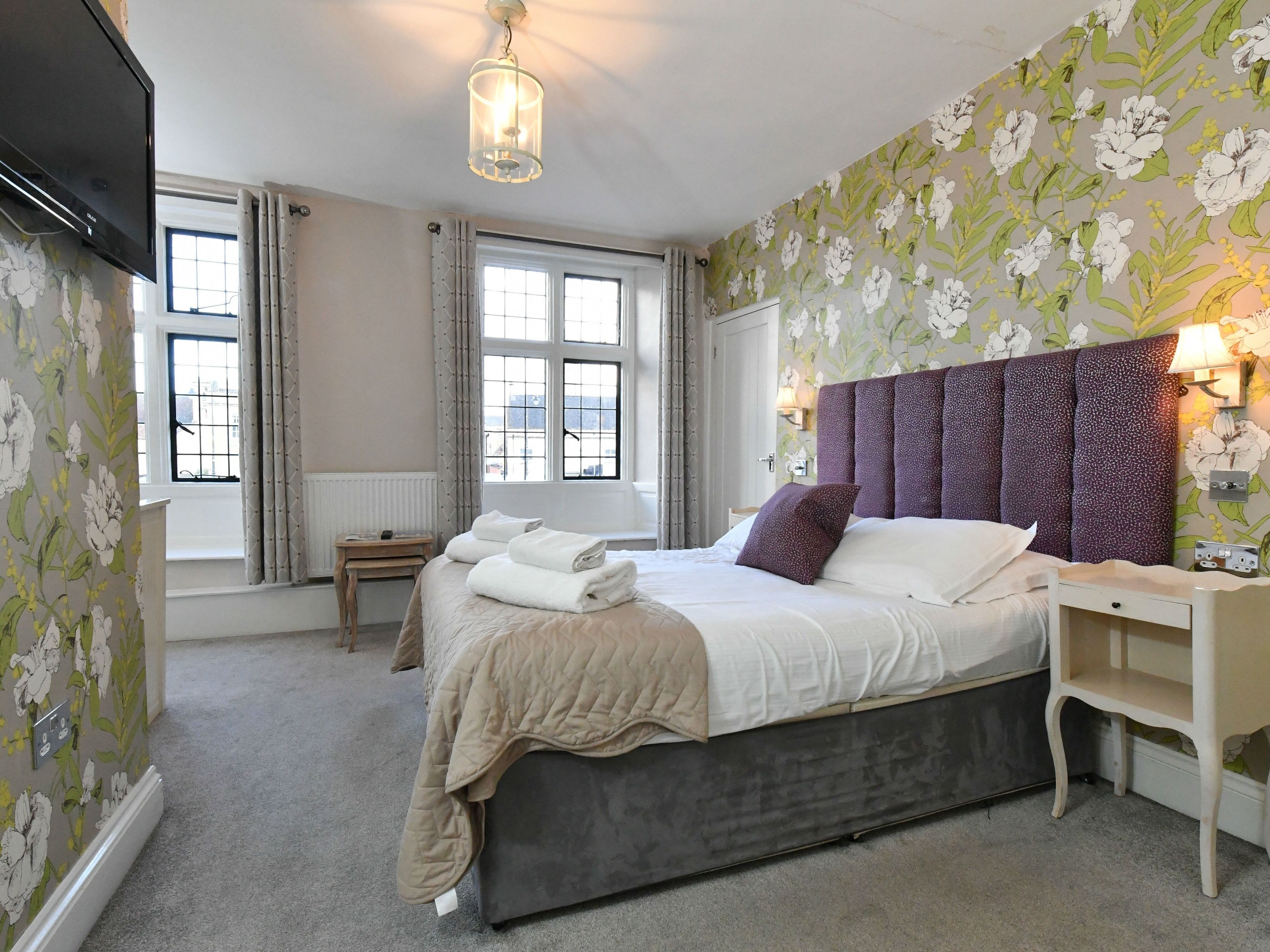 A bedroom with a bed, bedside table, lamp, and a TV.