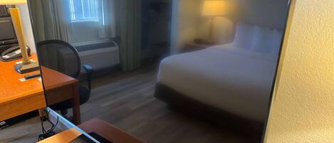 A hotel room with a bed, a desk with a lamp, a chair, and a television.