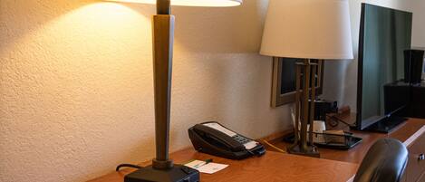 Escritorio de hotel con una lámpara, un teléfono, un control remoto y un espejo.
