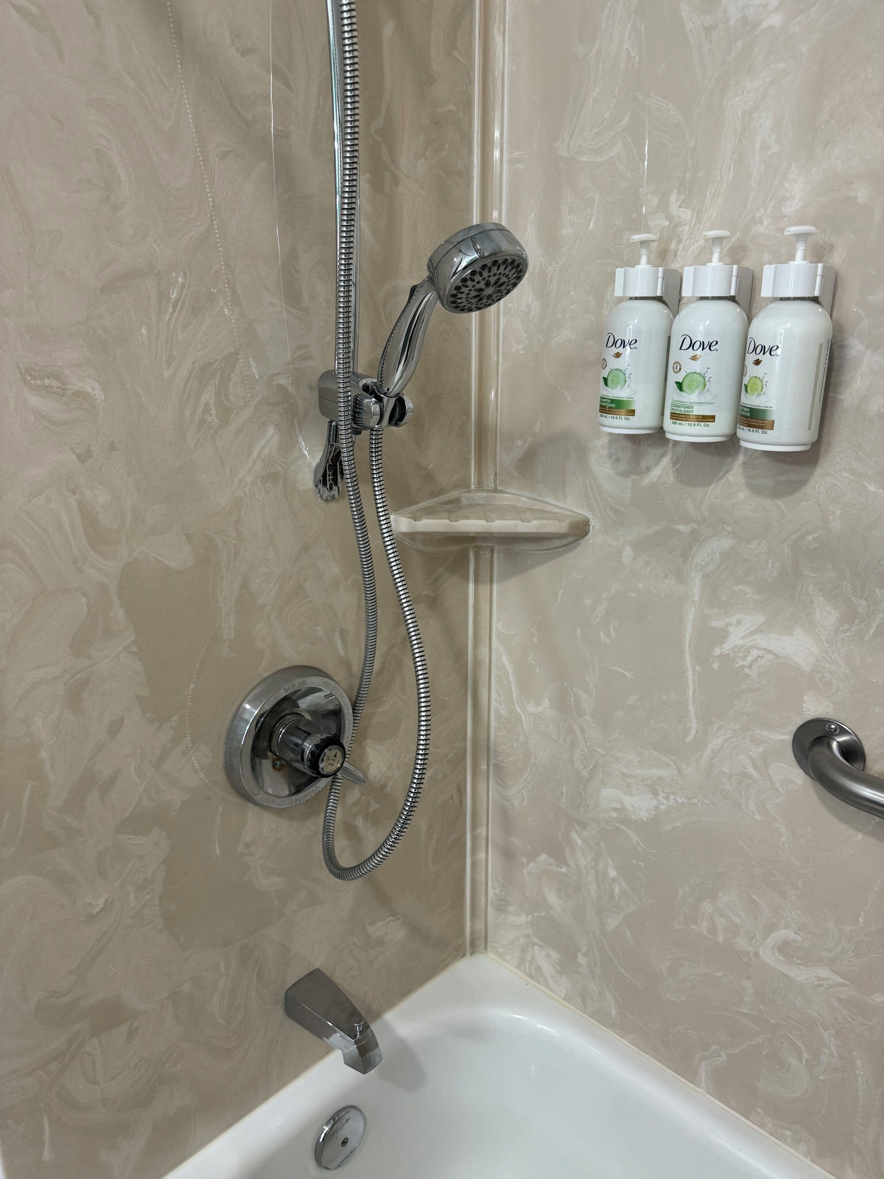 Ein Badezimmer mit Dusche, Badewanne und drei Dove Lotionflaschen auf einem Regal.