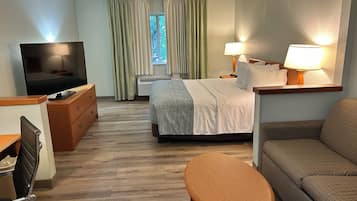 A hotel room with a bed, a television, a sofa, a small table, and a window with curtains.