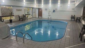 Una piscina interior con suelo de baldosas, una estación de socorristas y un área de estar con sillas.