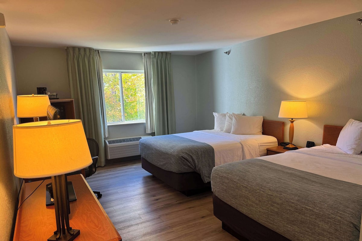 Habitación de hotel con dos camas, un escritorio con lámpara, un calentador y una ventana con cortinas.