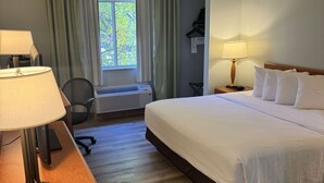Habitación de hotel con cama, dos lámparas de noche, un escritorio con lámpara, una silla, una ventana con cortinas y un calefactor de pared.