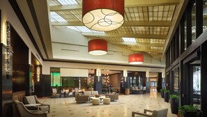A spacious lobby with a high ceiling, large windows, and modern lighting fixtures. - Hilton Rosemont Chicago O'Hare (Rosemont)