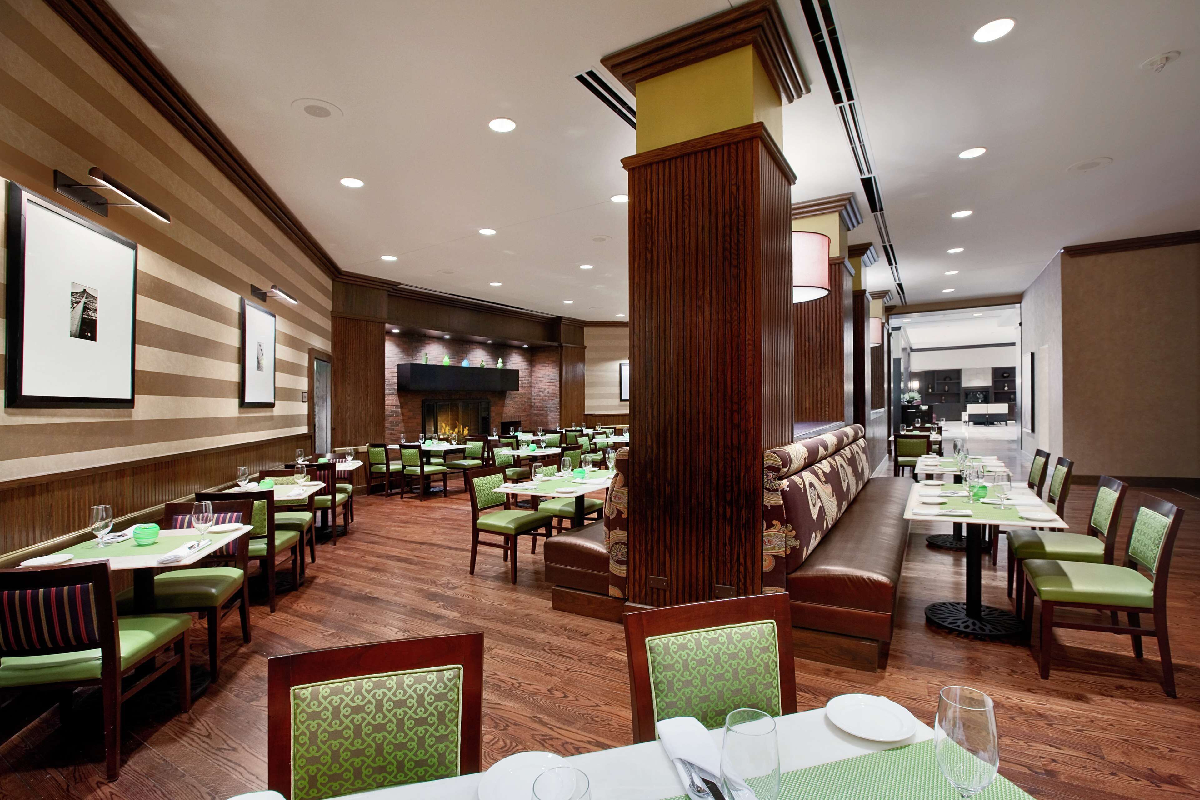 A spacious restaurant with multiple dining areas, green upholstered chairs, and wooden flooring.