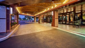 A hotel entrance with a covered walkway, glass doors, and outdoor seating. - Hilton Rosemont Chicago O'Hare (Rosemont)