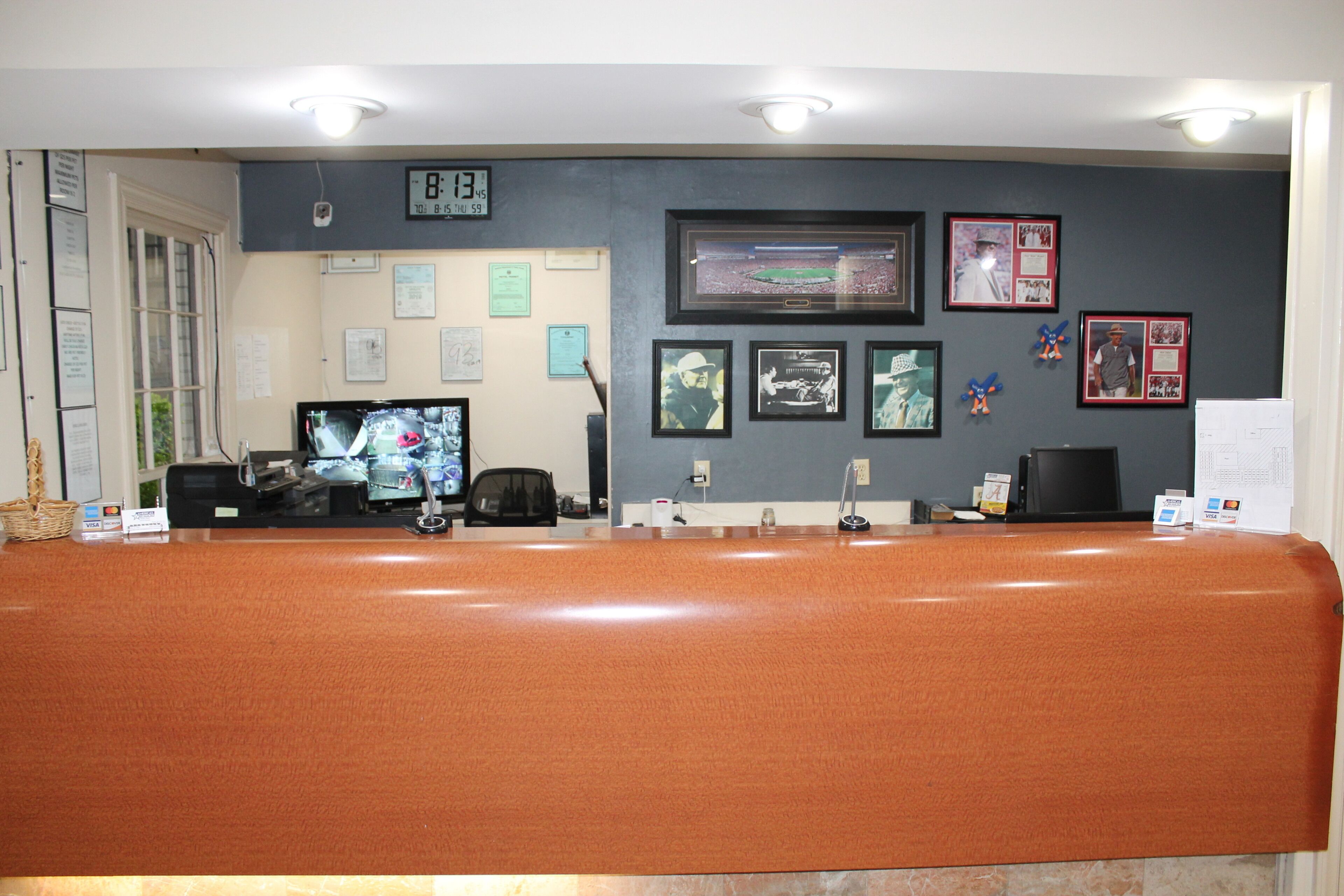 A reception area with a counter, computer monitors, framed pictures on the wall, and a clock.