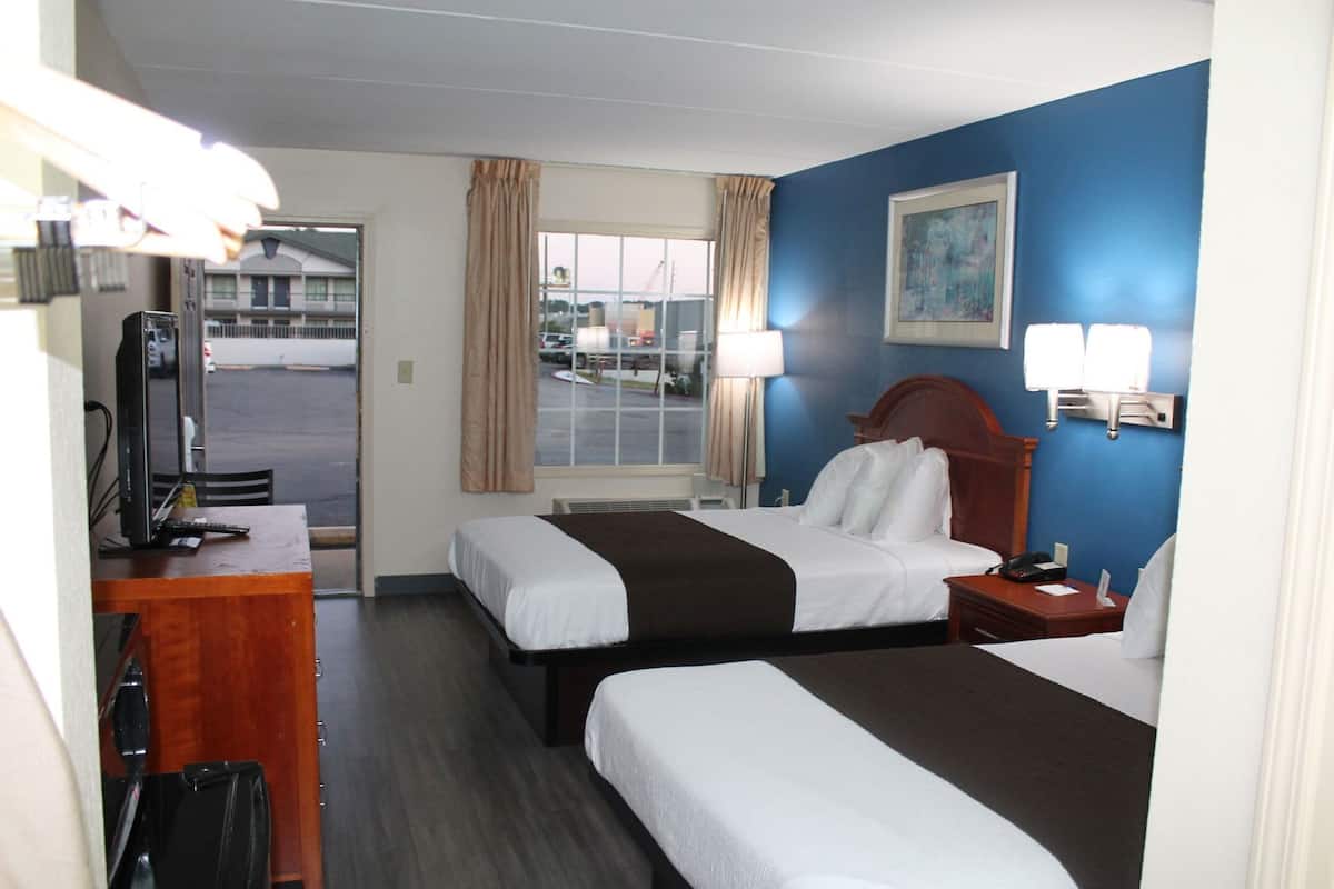 A hotel room with two beds, a desk with a computer, a lamp, and a painting on the wall.