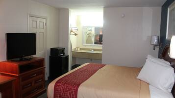 A hotel room with a bed, a TV on a wooden dresser, a bathroom with a sink and mirror, and a door.
