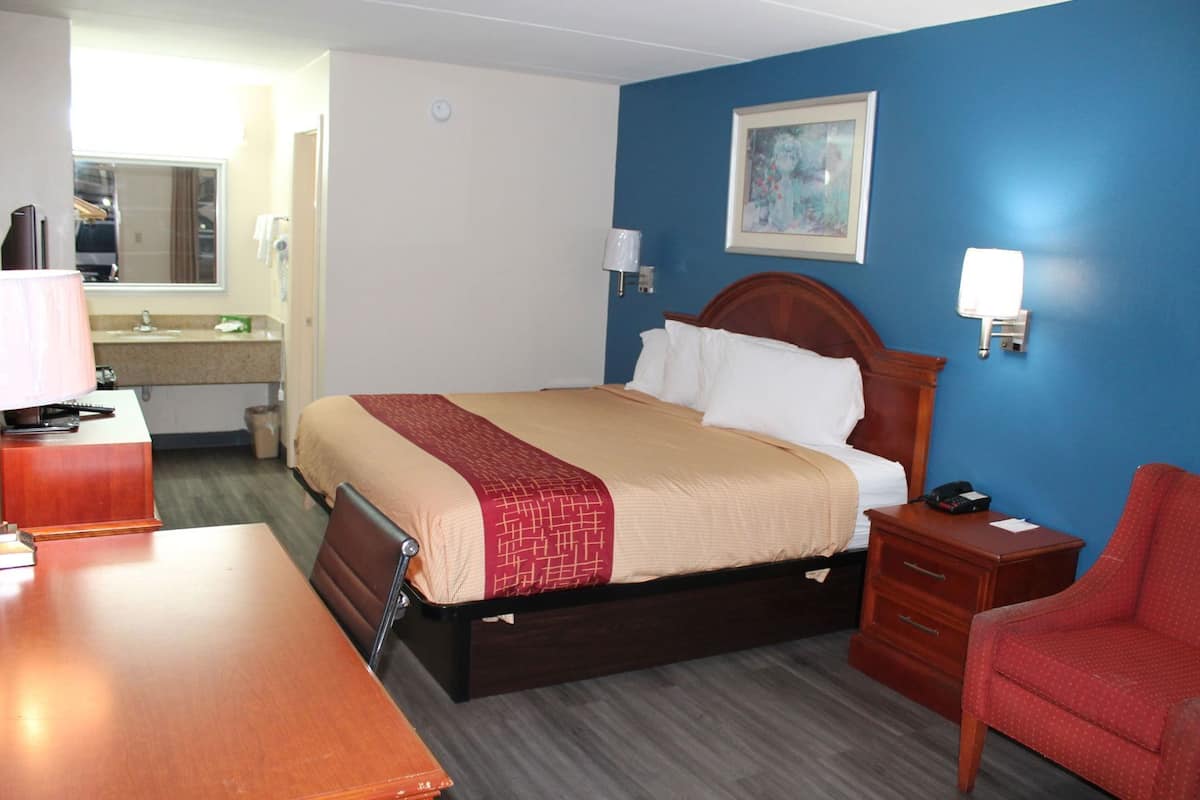 A hotel room with a bed, bedside table, chair, desk, and a bathroom visible through an open door.
