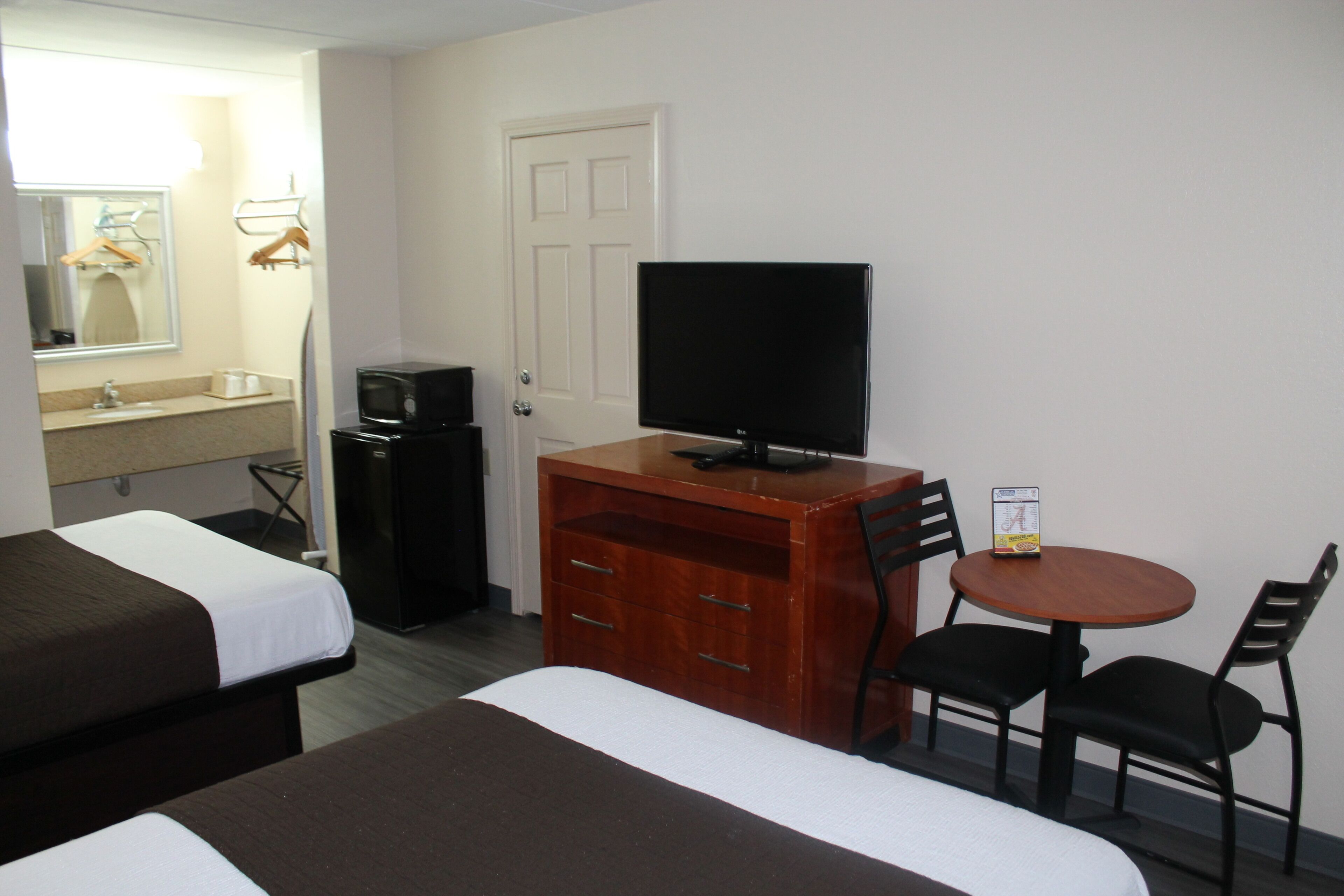 Een hotelkamer met twee bedden, een televisie, een bureau met stoel, en een kleine tafel met twee stoelen.