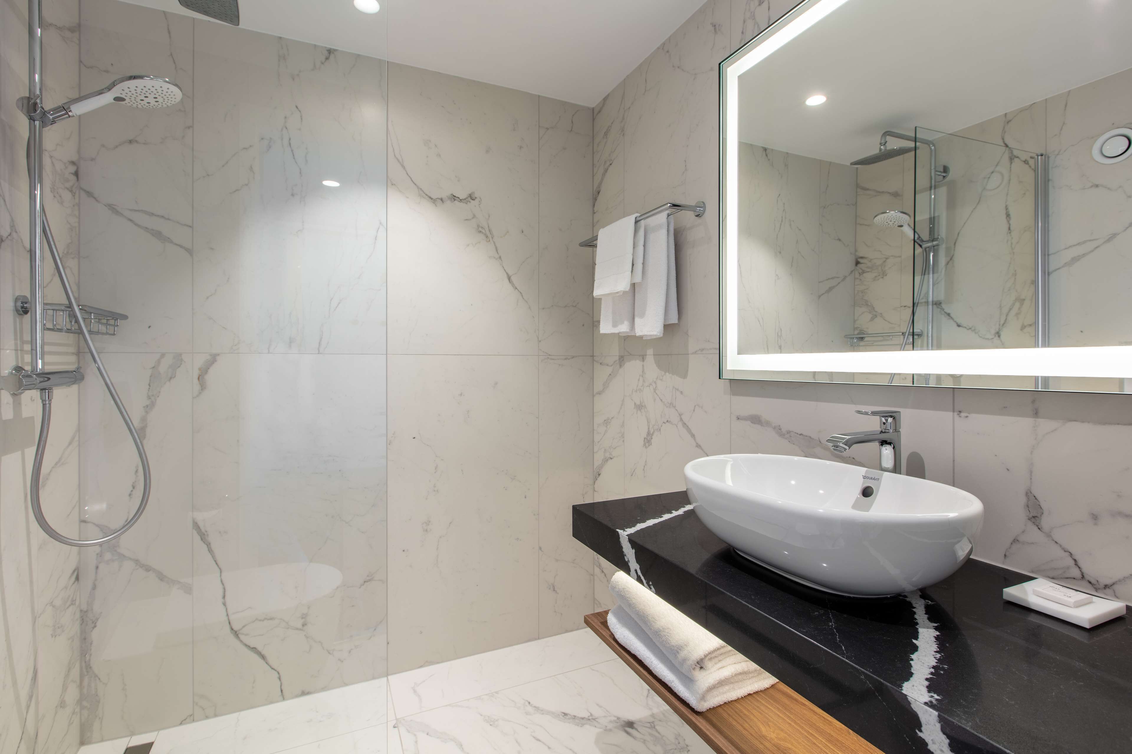 A modern bathroom with a marble floor, a white sink, a glass shower enclosure, and a large mirror.