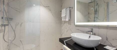 A modern bathroom with a marble floor, a white sink, a glass shower enclosure, and a large mirror.