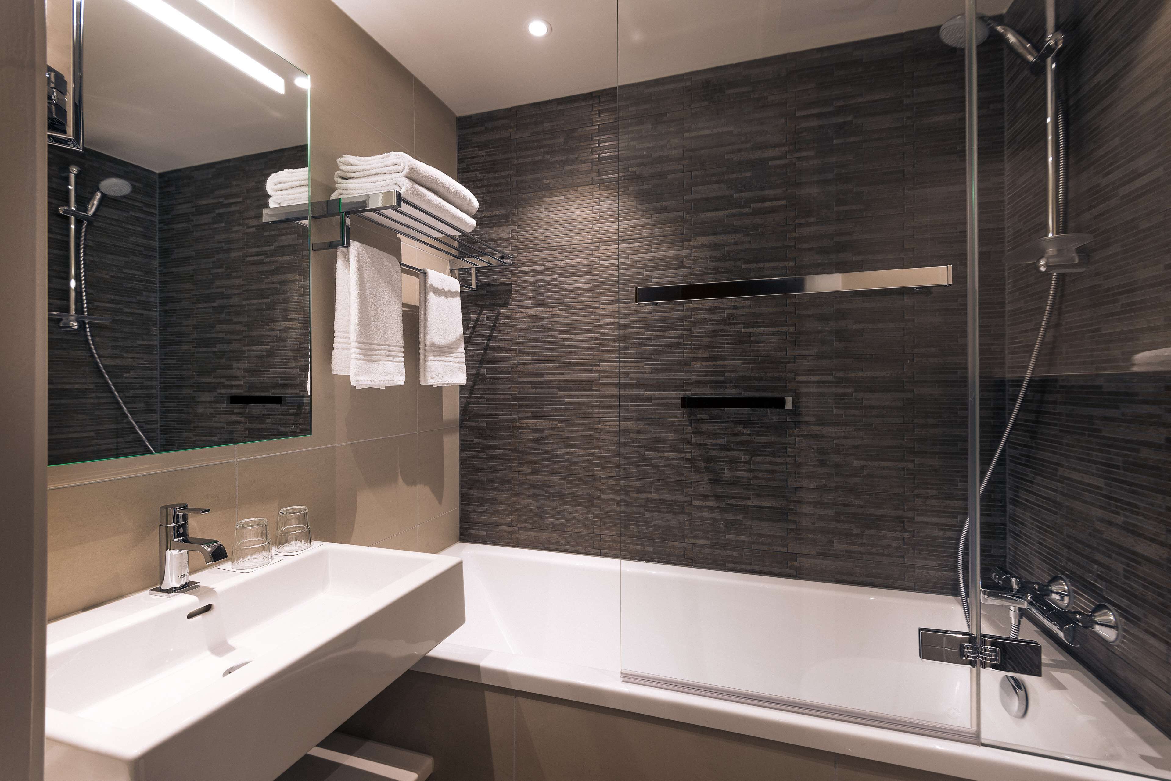Un baño moderno con ducha acristalada, un lavabo blanco y toallas ordenadas.