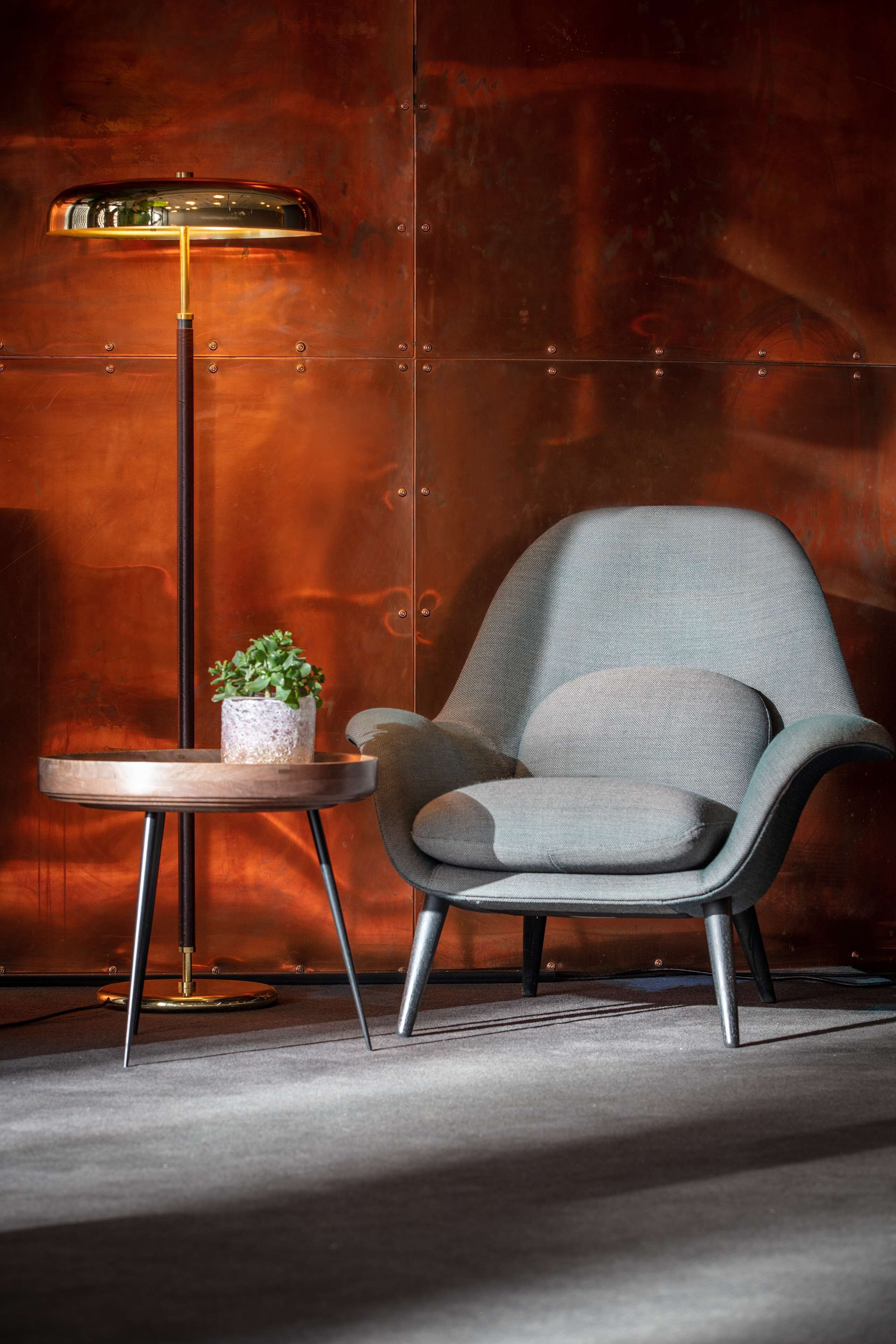 A modern armchair with a small side table and a floor lamp in a room with a metallic wall.