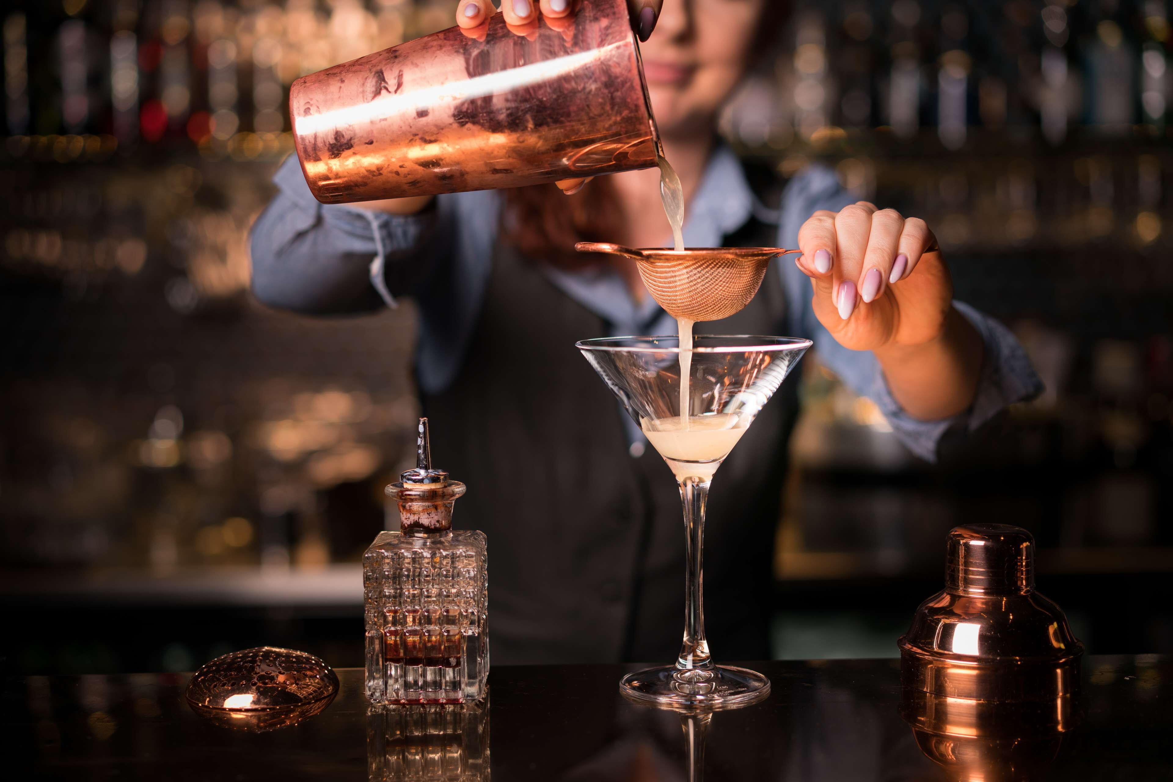 A bartender pouring a drink into a martini glass.