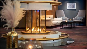 Un área de estar moderna con una chimenea central, asientos cómodos y un jarrón decorativo.