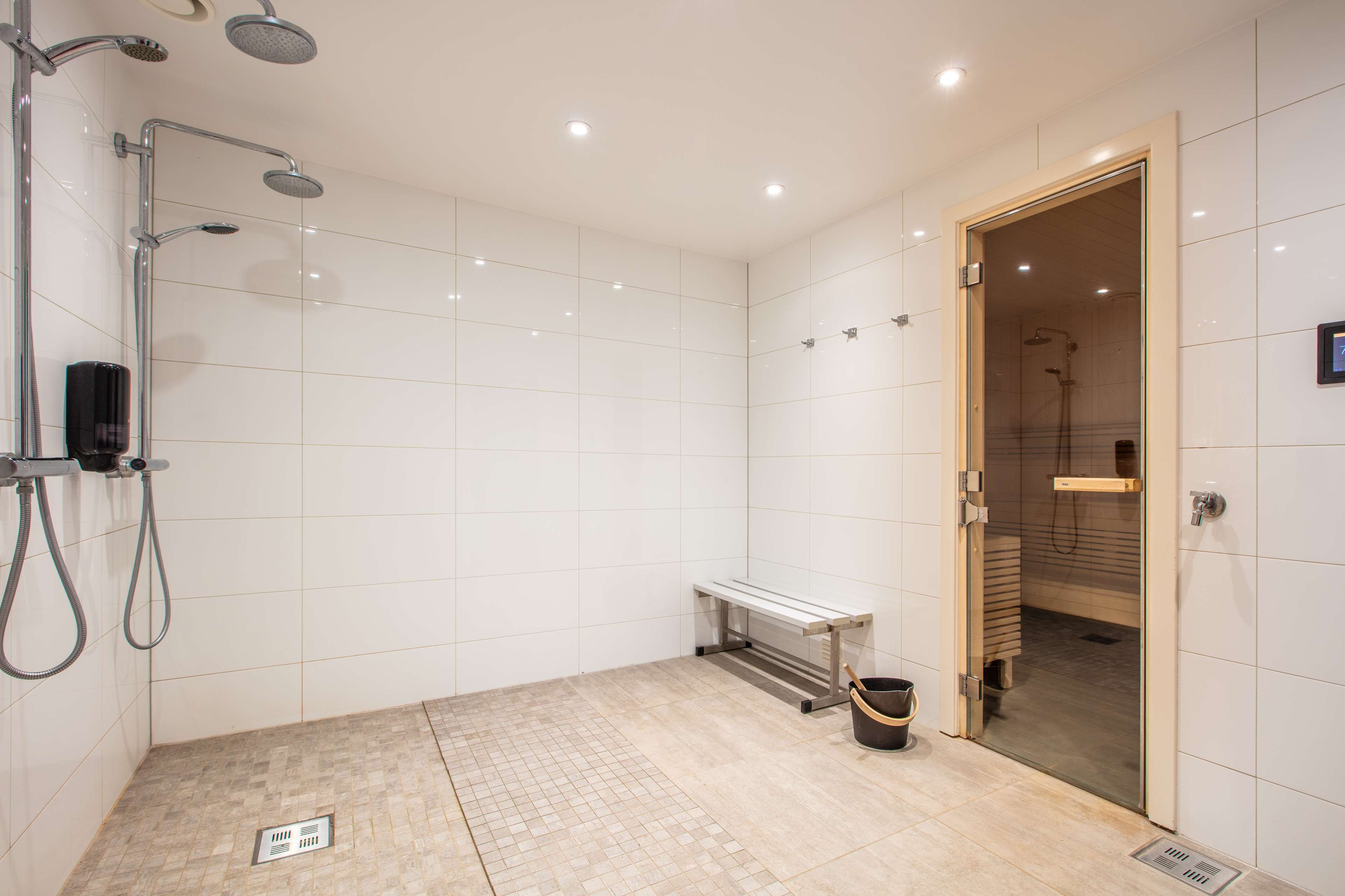 A modern bathroom with a shower, a bench, and a wooden door leading to a sauna.