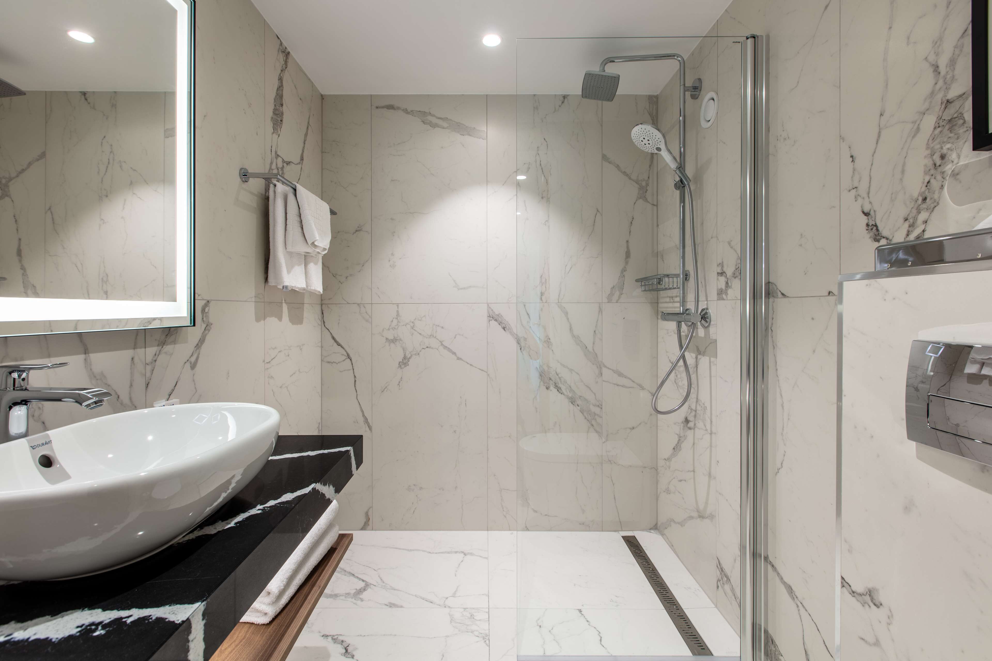 Une salle de bain moderne avec un grand lavabo blanc, une douche en verre et des murs en marbre.