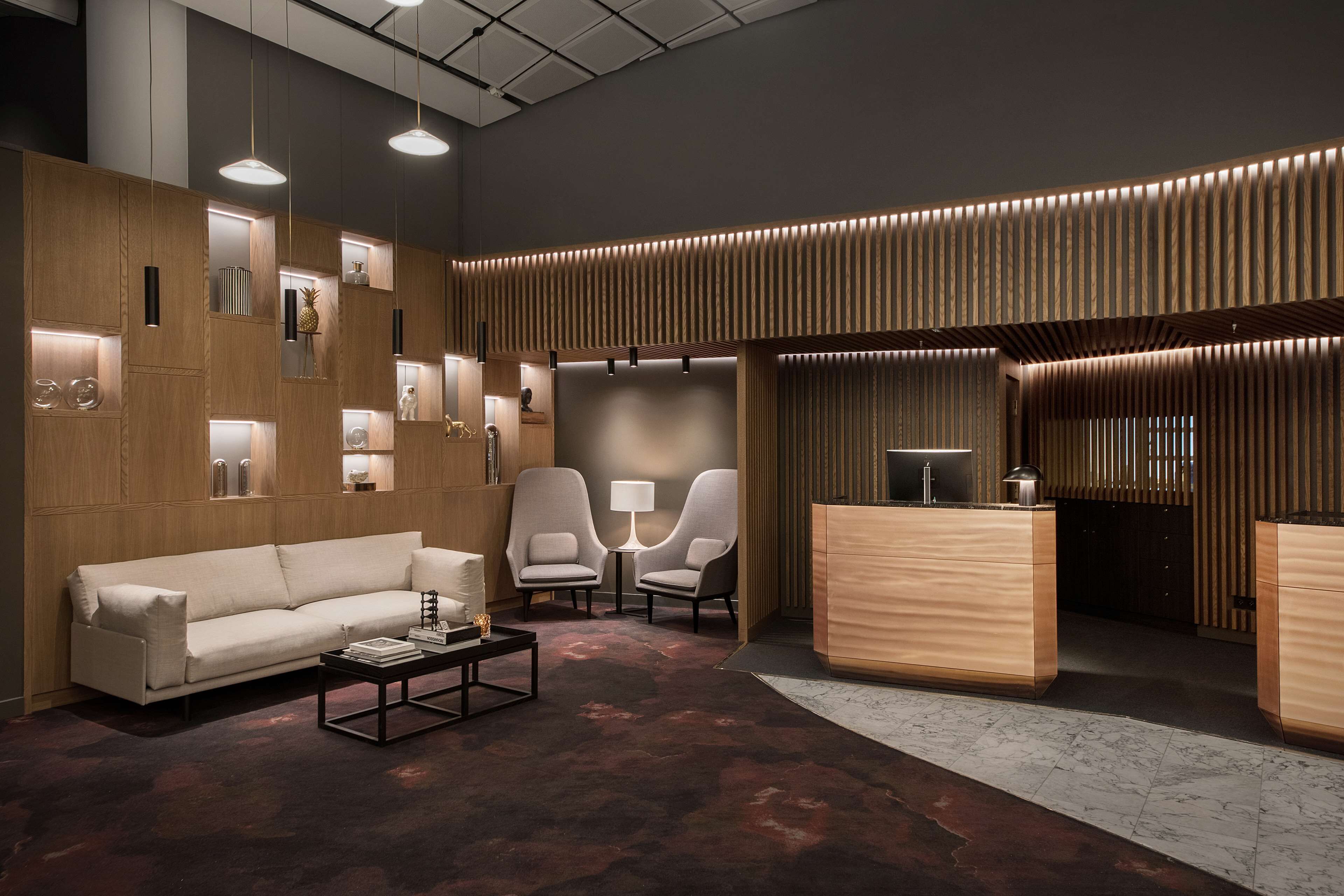 A modern lobby with a sofa, chairs, a reception desk, and a patterned wall.