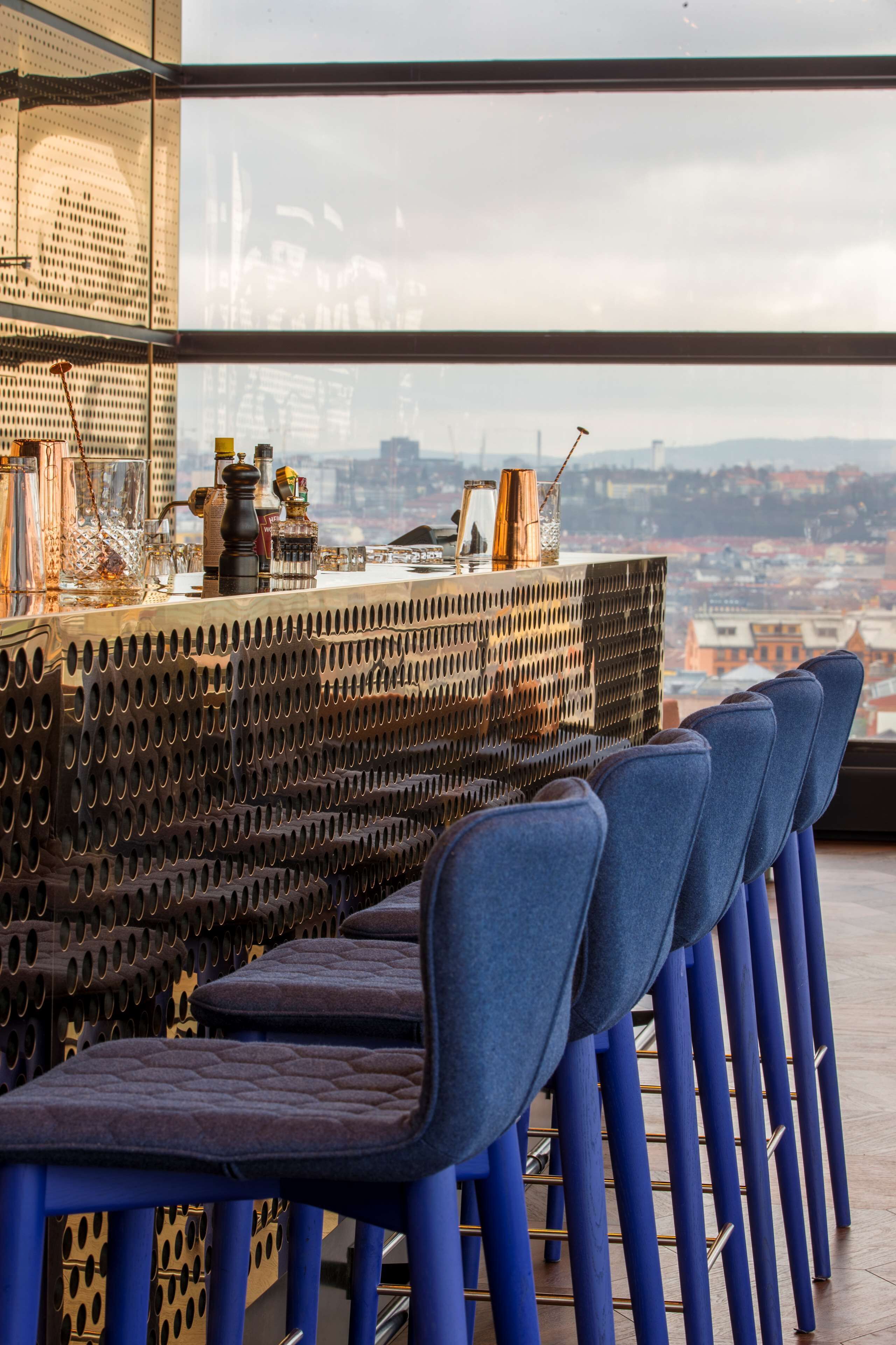Un espace bar avec des chaises bleues et une vue sur le paysage urbain, visible à travers de grandes fenêtres.