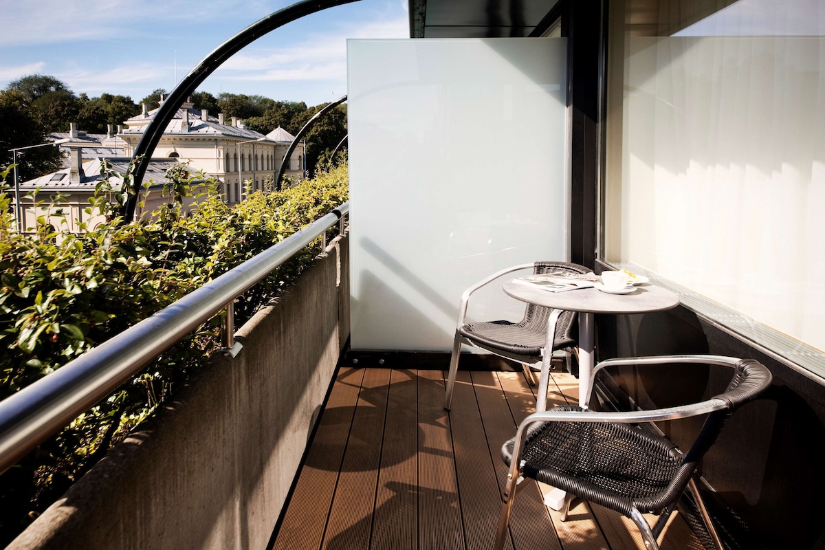 A balcony with a view of a building, a table with two chairs, and a railing.