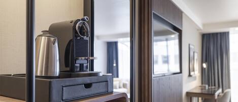 A hotel room with a wooden desk, a coffee maker, a mirror, and a view of the hallway.